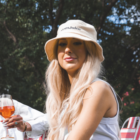 Woman sitting outdoors with a glass of wine, wearing a bucket hat and white top.