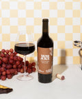 Cabernet Sauvignon on yellow checked background with red wine glass, grapes, chocolate, cork and cooking pan 