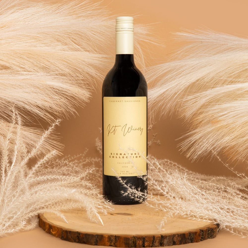 Wine bottle on a wooden coaster with decorative pampas grass against a beige background