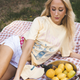 Woman sitting on a checkered blanket with a pie and bowl of lemons outdoors