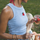 Woman in light blue sleeveless top with strawberry design, holding a drink outdoors.