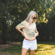 Woman standing on a checkered blanket in a park wearing a graphic t-shirt and sunglasses.