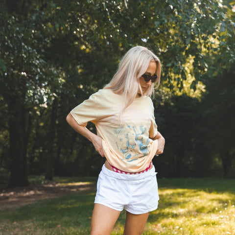 Woman standing on a checkered blanket in a park wearing a graphic t-shirt and sunglasses.