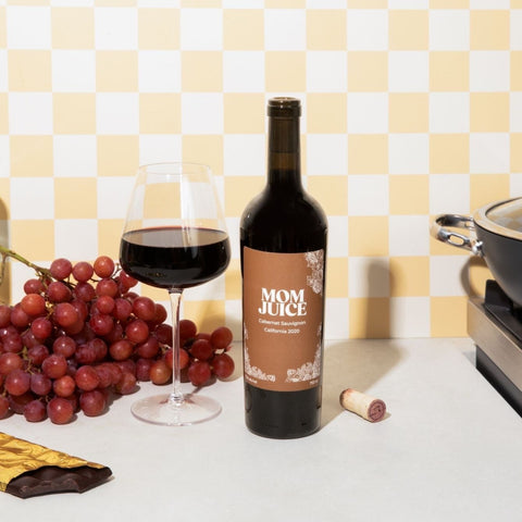 Cabernet Sauvignon on yellow checked background with red wine glass, grapes, chocolate, cork and cooking pan 