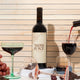 Editorial photo of mom juice red blend on wooden background, tipped wine glasses, full wine glass and more wine pouring